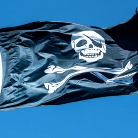 Black Jolly Roger skull-and-crossbones pirate flag flying against a blue sky — Halloween flags in Colorado